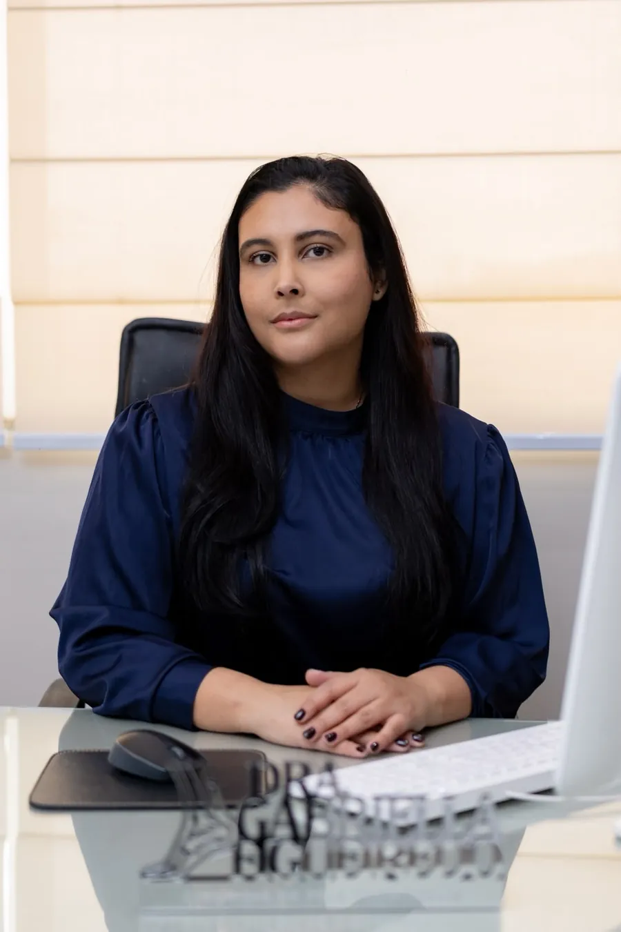 Dra. Gabriella Figueiredo sentada à mesa do consultório, em frente ao computador, durante atendimento por teleconsulta
